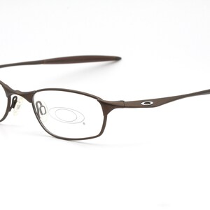 May include: Brown metal frame eyeglasses with clear lenses. The brand name "Oakley" is visible on the right temple.