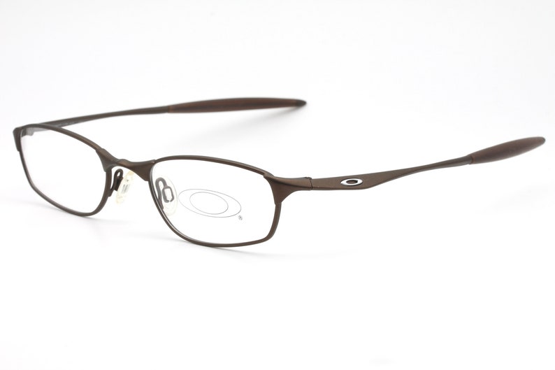 May include: Brown metal frame eyeglasses with clear lenses. The brand name "Oakley" is visible on the right temple.
