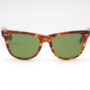 May include: Sunglasses with a classic design. The frames are a tortoiseshell pattern, with a mix of brown and amber hues. The lenses are a solid green color. The sunglasses are set against a white background.