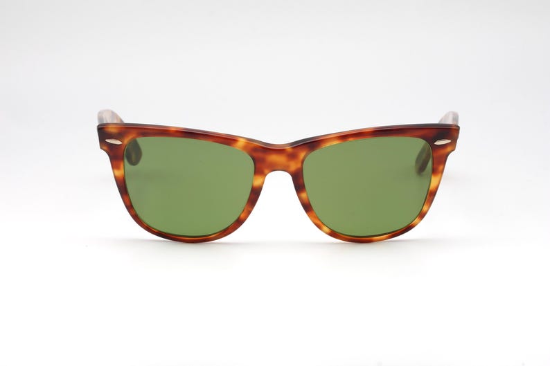 May include: Sunglasses with a classic design. The frames are a tortoiseshell pattern, with a mix of brown and amber hues. The lenses are a solid green color. The sunglasses are set against a white background.