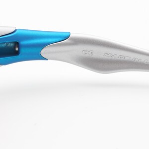 May include: Close-up of the silver arm of a pair of sunglasses with a blue accent. The arm is marked with "Made in U.S.A."