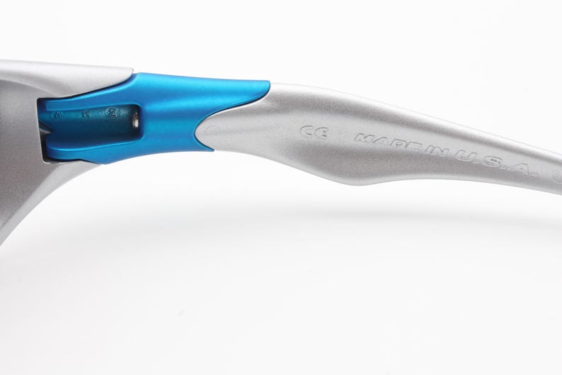 May include: Close-up of the silver arm of a pair of sunglasses with a blue accent. The arm is marked with "Made in U.S.A."