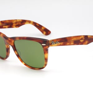 May include: Tortoiseshell-framed sunglasses with green lenses. The sunglasses have a classic design with a brown and amber pattern on the frames and arms. The Ray-Ban logo is visible on the right arm.