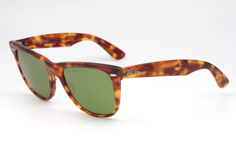 May include: Tortoiseshell-framed sunglasses with green lenses. The sunglasses have a classic design with a brown and amber pattern on the frames and arms. The Ray-Ban logo is visible on the right arm.