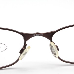 May include: Close-up of a pair of brown metal eyeglasses with clear lenses. The glasses have a unique oval shape and the arms are marked with "52 20".