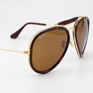 May include: Brown aviator sunglasses with a gold-tone metal frame. The lenses are a warm brown color, and the frames have a tortoiseshell pattern. The Ray-Ban logo is visible on the lens.
