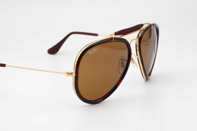 May include: Brown aviator sunglasses with a gold-tone metal frame. The lenses are a warm brown color, and the frames have a tortoiseshell pattern. The Ray-Ban logo is visible on the lens.