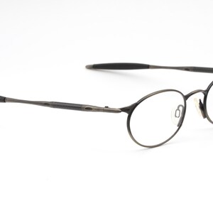 May include: A pair of round, black metal eyeglasses with thin frames. The glasses have a subtle, almost brushed, finish.
