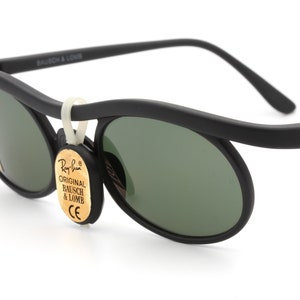 May include: Black Ray-Ban sunglasses with green lenses and a gold tag that reads "Original Bausch & Lomb".