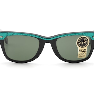 Puede incluir: Gafas de sol Ray-Ban negras con monturas de patr&oacute;n verde y negro. Las gafas tienen lentes verdes y una pegatina dorada que dice "Ray-Ban G-15 Lens".