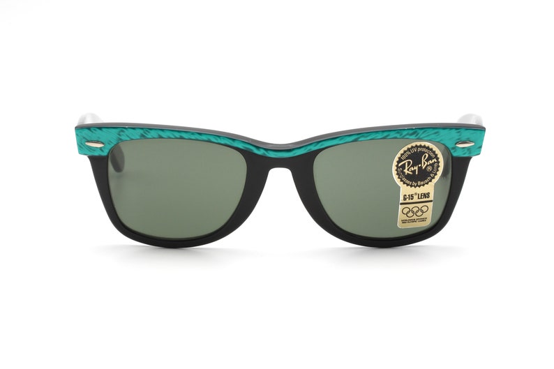 Puede incluir: Gafas de sol Ray-Ban negras con monturas de patr&oacute;n verde y negro. Las gafas tienen lentes verdes y una pegatina dorada que dice "Ray-Ban G-15 Lens".