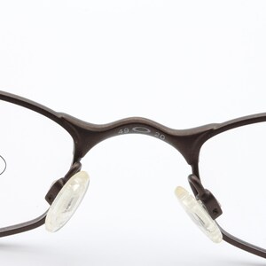May include: Close-up of brown eyeglasses with clear lenses. The frame has a dark brown color and features clear nose pads. The bridge of the glasses has the numbers "49 20" printed on it. The glasses are designed for vision correction.