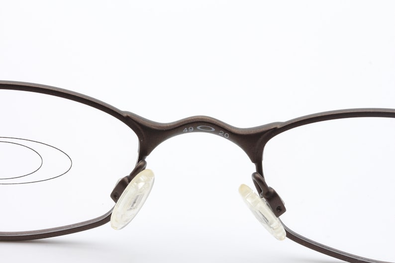 May include: Close-up of brown eyeglasses with clear lenses. The frame has a dark brown color and features clear nose pads. The bridge of the glasses has the numbers "49 20" printed on it. The glasses are designed for vision correction.
