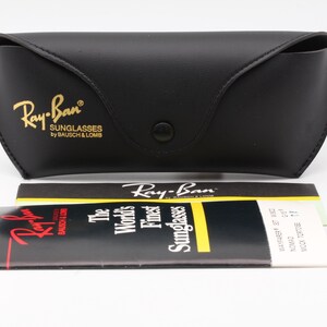 Puede incluir: Estuche negro para gafas de sol Ray-Ban con letras doradas y cierre a presi&oacute;n. El estuche va acompa&ntilde;ado de un folleto y una tarjeta plegada con el logotipo y el texto de Ray-Ban. El texto del folleto dice "Las mejores gafas de sol del mundo".