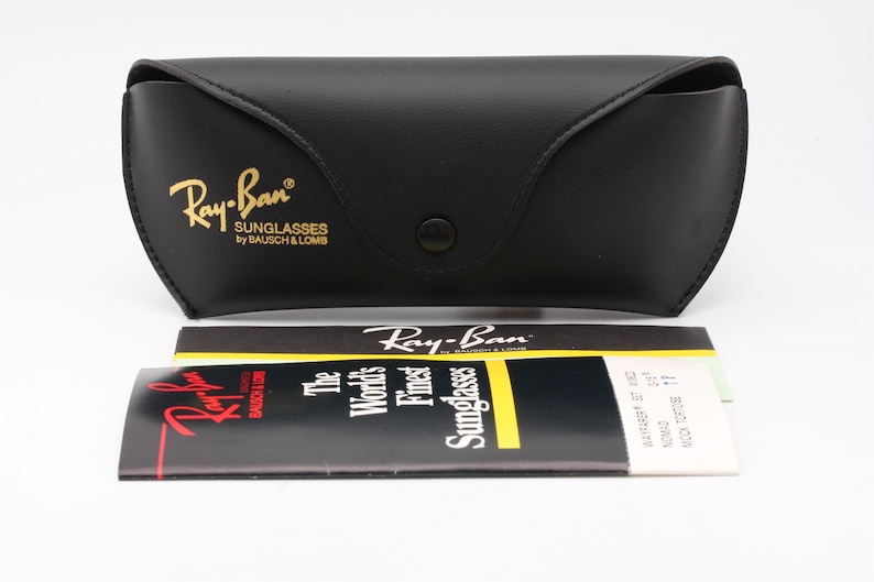 Puede incluir: Estuche negro para gafas de sol Ray-Ban con letras doradas y cierre a presi&oacute;n. El estuche va acompa&ntilde;ado de un folleto y una tarjeta plegada con el logotipo y el texto de Ray-Ban. El texto del folleto dice "Las mejores gafas de sol del mundo".