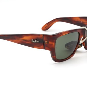 Puede incluir: Gafas de sol Ray-Ban con estampado de carey y lentes verdes. Las gafas tienen una montura rectangular y un dise&ntilde;o cl&aacute;sico. El logotipo de Ray-Ban es visible en la patilla. Una etiqueta blanca est&aacute; adjunta.