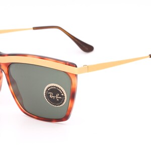 May include: Tortoise shell frame sunglasses with gold accents and green lenses. The sunglasses have a Ray-Ban logo on the right lens.