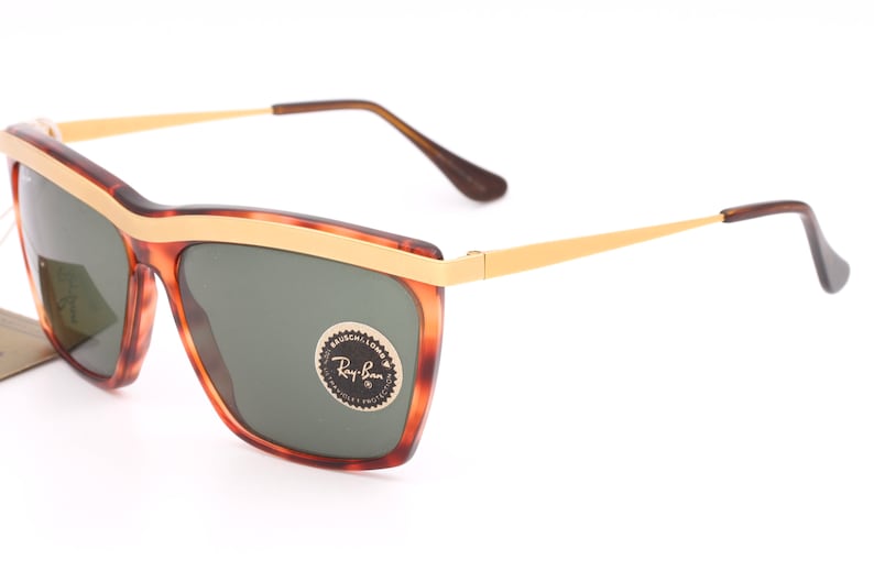 May include: Tortoise shell frame sunglasses with gold accents and green lenses. The sunglasses have a Ray-Ban logo on the right lens.