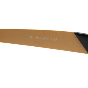 Puede incluir: Primer plano del brazo dorado de unas gafas de sol Ray-Ban. El brazo est&aacute; inscrito con "B&L RAY-BAN USA".