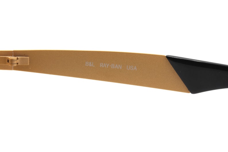 Puede incluir: Primer plano del brazo dorado de unas gafas de sol Ray-Ban. El brazo est&aacute; inscrito con "B&L RAY-BAN USA".