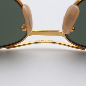 May include: Gold-tone Ray-Ban sunglasses with green lenses and a gold metal frame. The sunglasses have a "58L RAY-BAN 52014" inscription on the frame.