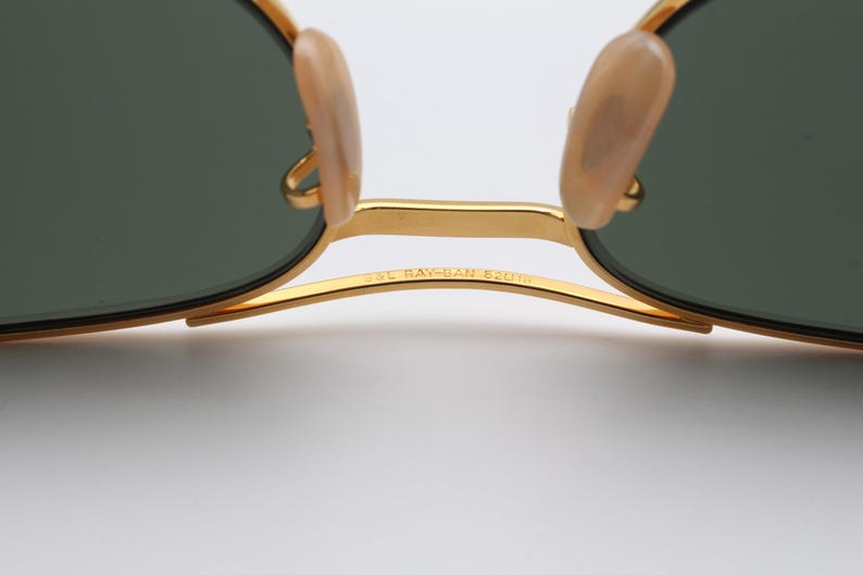 May include: Gold-tone Ray-Ban sunglasses with green lenses and a gold metal frame. The sunglasses have a "58L RAY-BAN 52014" inscription on the frame.