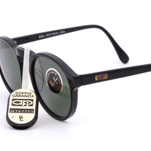 May include: Black round Ray-Ban sunglasses with green lenses. The sunglasses have a gold Ray-Ban logo on the right arm and the text "B&L Ray-Ban USA" on the left arm.
