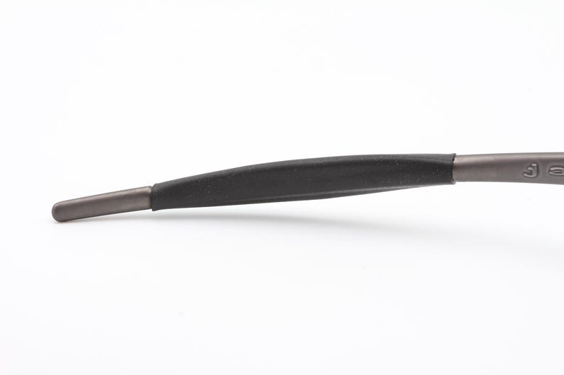 May include: Close-up of the temple arm of a pair of eyeglasses. The arm is a dark gray color with a black rubber grip. The tip of the arm is a lighter gray color.