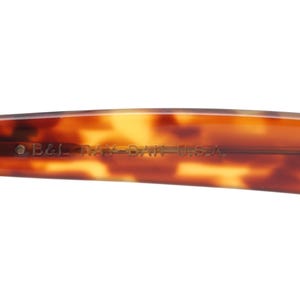 May include: Close-up of the arm of a pair of sunglasses with a tortoiseshell pattern. The text "B&L RAY-BAN U.S.A." is printed on the arm. The hinge is visible on the left side of the frame.