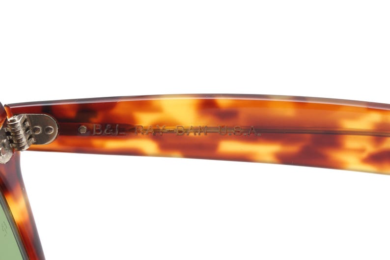 May include: Close-up of the arm of a pair of sunglasses with a tortoiseshell pattern. The text "B&L RAY-BAN U.S.A." is printed on the arm. The hinge is visible on the left side of the frame.