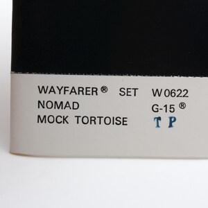 Puede incluir: Primer plano de una etiqueta de producto con fondo blanco, texto negro y una parte superior negra. El texto incluye "WAYFARER SET W 0622 NOMAD MOCK TORTOISE G-15 TP".