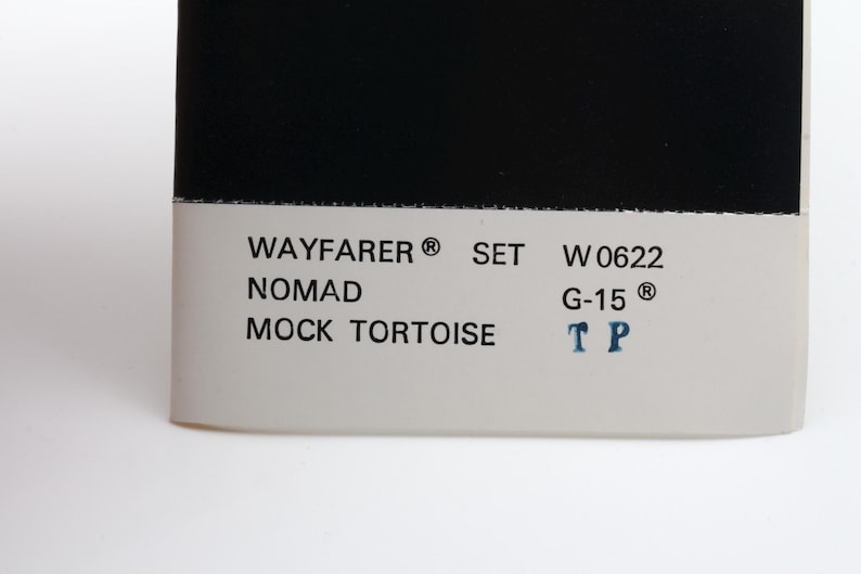Puede incluir: Primer plano de una etiqueta de producto con fondo blanco, texto negro y una parte superior negra. El texto incluye "WAYFARER SET W 0622 NOMAD MOCK TORTOISE G-15 TP".