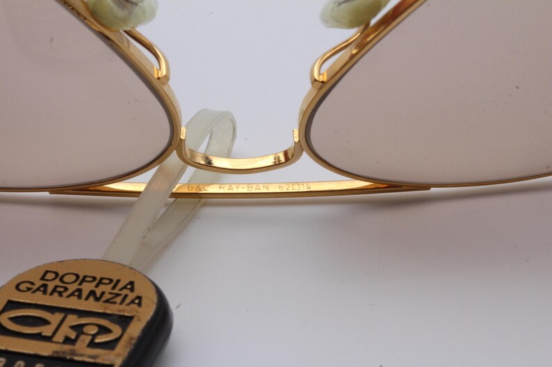 May include: Close-up of gold-tone aviator sunglasses with a brown lens. The sunglasses have the text "B&L Ray-Ban 6211" engraved on the frame.