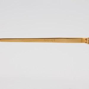 May include: Gold-tone metal sunglasses with green lenses. The sunglasses have a Signet inscription on the arm.