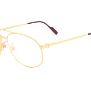 May include: Gold aviator eyeglasses with clear lenses and burgundy temple tips.