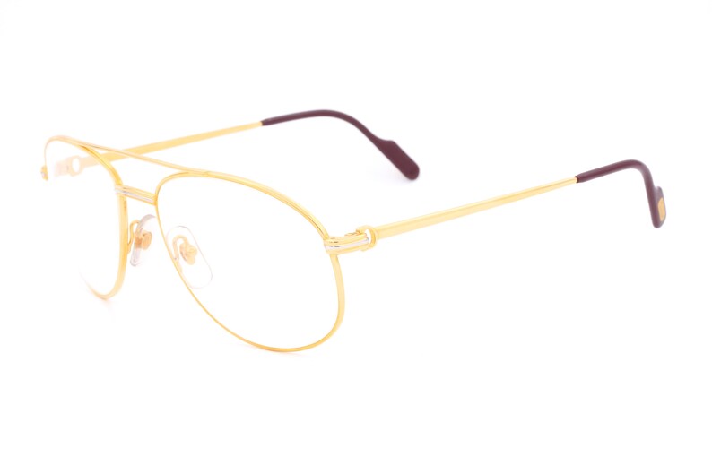 May include: Gold aviator eyeglasses with clear lenses and burgundy temple tips.