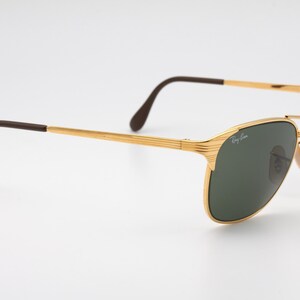 May include: Gold-tone aviator sunglasses with green lenses and brown temple tips. The sunglasses have a Ray-Ban logo on the right lens.