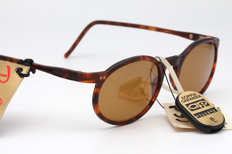 May include: Brown tortoise shell round sunglasses with brown lenses. The sunglasses have a gold metal accent on the side. The sunglasses are attached to a white string and have a tag that says "Doppia Garanzia" with a logo and the number "2745865".