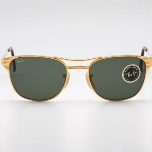 May include: Gold-tone aviator sunglasses with green lenses and a Ray-Ban logo on the side.