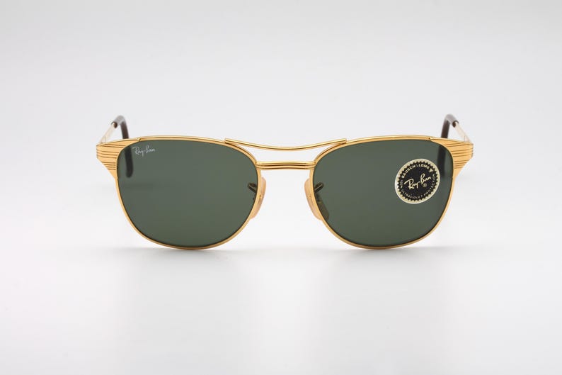 May include: Gold-tone aviator sunglasses with green lenses and a Ray-Ban logo on the side.