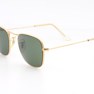 May include: Gold-framed sunglasses with green lenses. The sunglasses have a classic, rectangular shape.