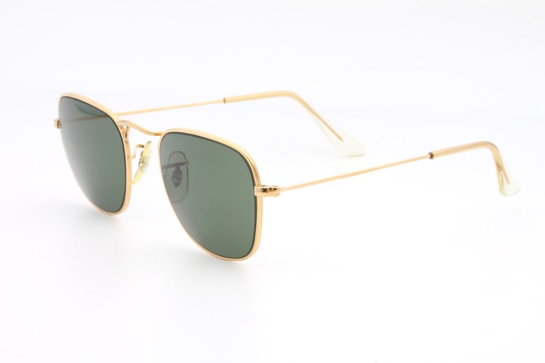 May include: Gold-framed sunglasses with green lenses. The sunglasses have a classic, rectangular shape.