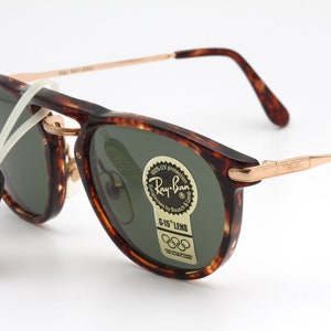 Op de afbeelding: Schildpad Ray-Ban zonnebril met groene glazen en gouden accenten. De zonnebril heeft een Ray-Ban logo aan de zijkant en een G-15 lens sticker met de Olympische ringen.