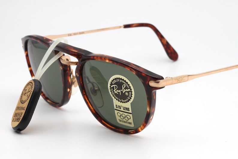 Op de afbeelding: Schildpad Ray-Ban zonnebril met groene glazen en gouden accenten. De zonnebril heeft een Ray-Ban logo aan de zijkant en een G-15 lens sticker met de Olympische ringen.