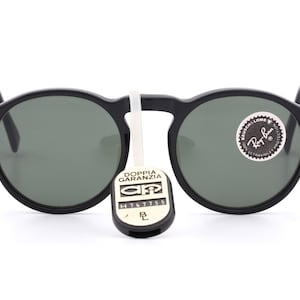 May include: Black round sunglasses with green lenses. The sunglasses have a Ray-Ban logo on the right lens and a tag that says "Doppia Garanzia" with a serial number.