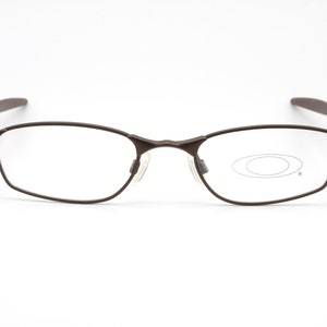 May include: Brown metal frame eyeglasses with clear lenses. The brand name "Oakley" is visible on the right temple.