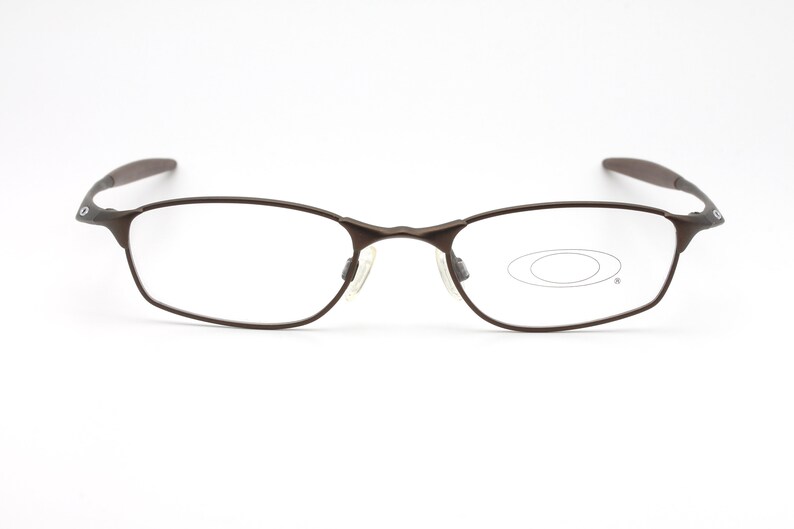 May include: Brown metal frame eyeglasses with clear lenses. The brand name "Oakley" is visible on the right temple.