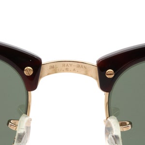 Może przedstawiać: Zbliżenie na złoty metalowy mostek brązowych okular&oacute;w przeciwsłonecznych Ray-Ban w kolorze ż&oacute;łwim. Mostek jest grawerowany napisem "B&L RAY-BAN U.S.A."