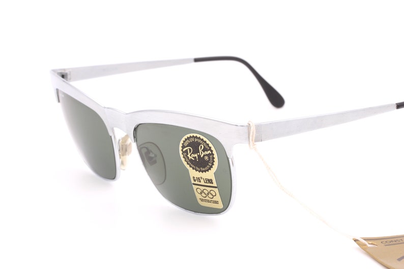 May include: Silver Ray-Ban sunglasses with green lenses and a G-15 lens label. The sunglasses have a thin, white string attached to the frame.