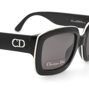 May include: Black square sunglasses with a silver trim and the text "Christian Dior" on the lens. The sunglasses have a silver "CD" logo on the side.